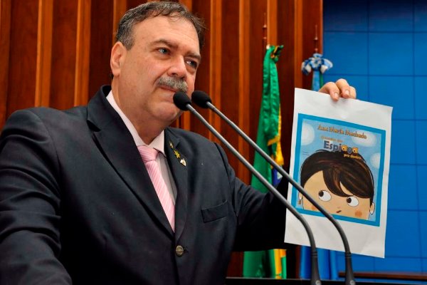 Imagem: Deputado Dr. Paulo Siufi, com cópia da capa do livro O Menino que Espiava pra Dentro: "Obra vergonhosa que incita nossas crianças"