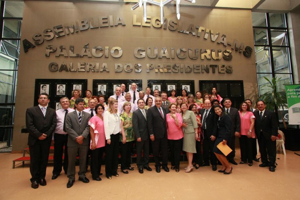 Imagem: Deputados estaduais posam para foto com Coral da ALMS no saguão.